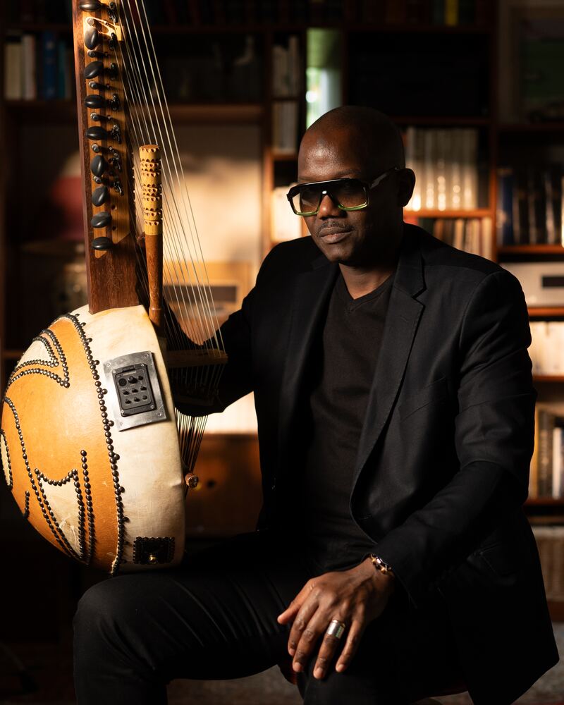 Kourou Fia assis près de sa kora, dans une lumière chaude. — Kourou Fia seated beside his kora, in warm light.