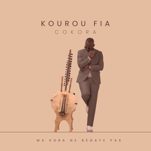Pochette de COKORA : Kourou Fia debout près de sa kora, sur fond sable. « Ma kora ne bégaye pas ».